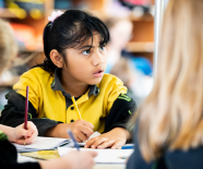 Child sitting at a desk holding a pencil.